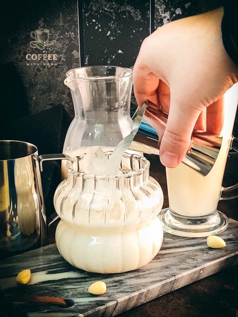 Pouring the almond syrup to the glass filled with almond milk and ice cubes.