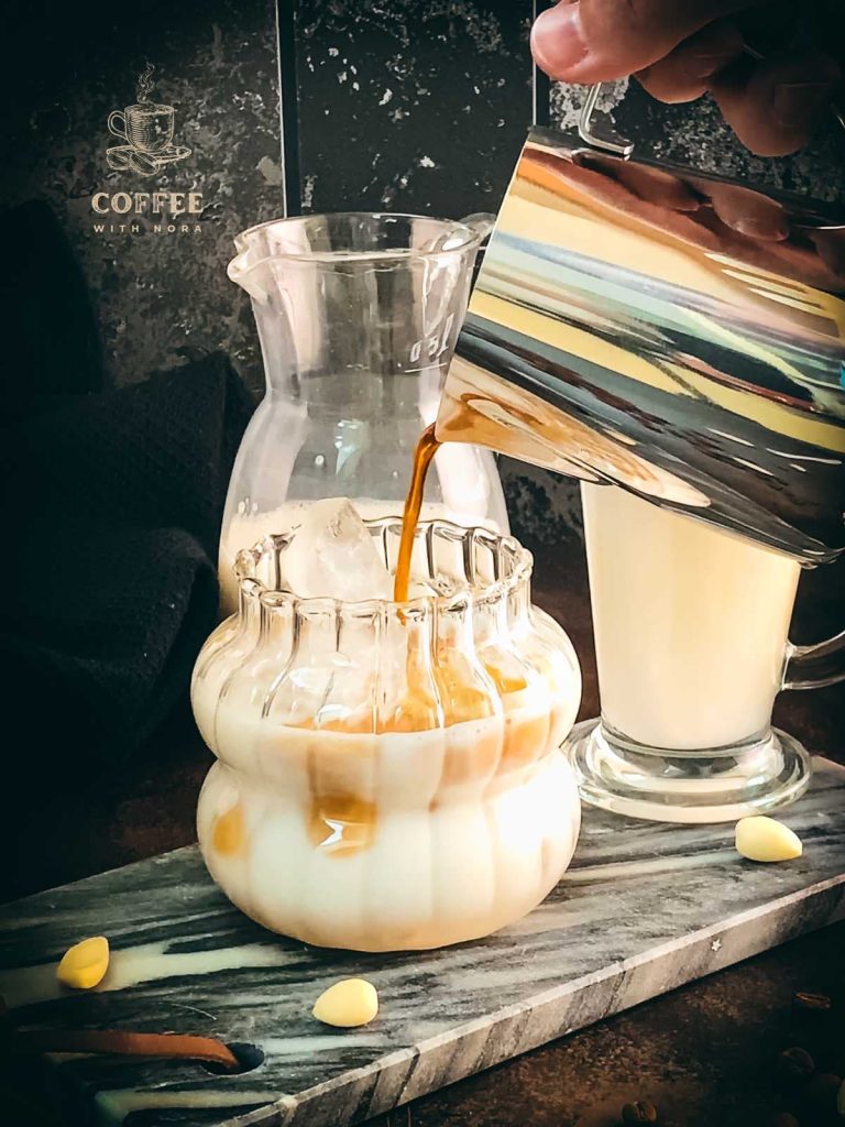 Pouring the strong coffee to the glass filled with almond milk and ice cubes.