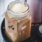 Mason jar filled with delicious iced coffee with vanilla ice cream, placed on a black plate.