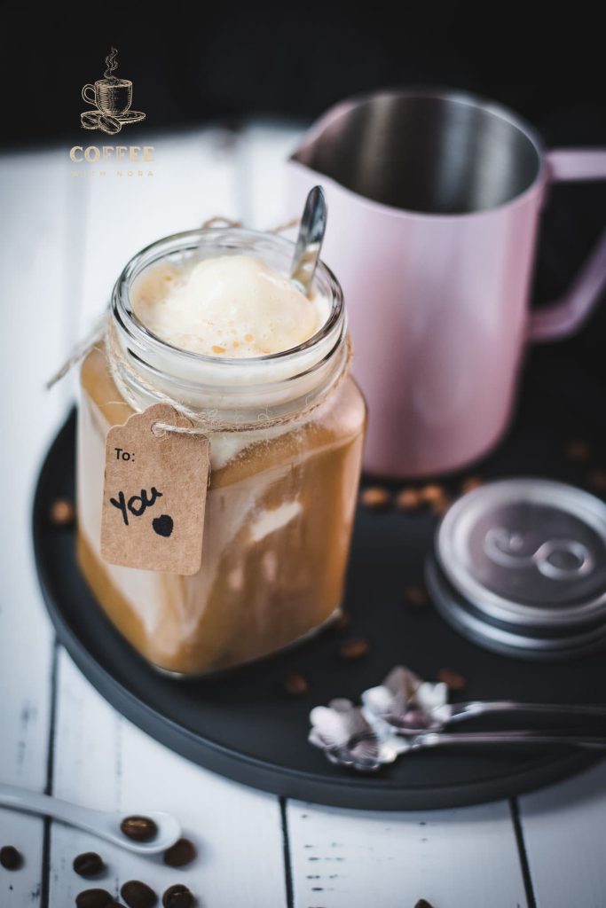 Mason jar filled with delicious iced coffee with vanilla ice cream, placed on a black plate.