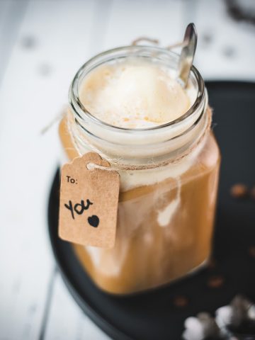 Mason jar filled with delicious iced coffee with vanilla ice cream, placed on a black plate.