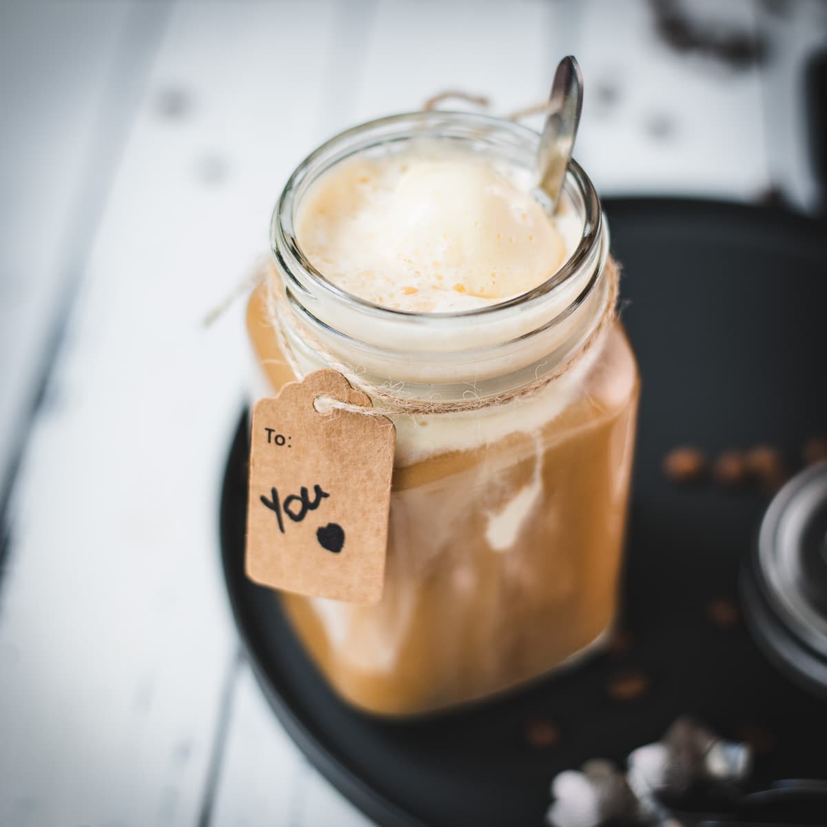 Mason jar filled with delicious iced coffee with vanilla ice cream, placed on a black plate.