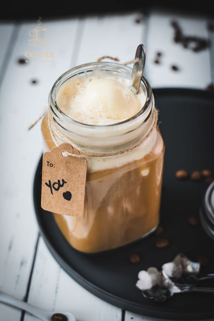 Mason jar filled with delicious iced coffee with vanilla ice cream, placed on a black plate.