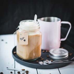 Mason jar filled with delicious iced coffee with vanilla ice cream, placed on a black plate.