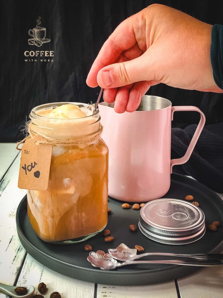 Hand placing a spoon into the mason jar filled with vanilla iced coffee.