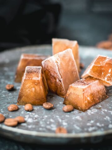 Frozen coffee cubes placed on metal plate next to coffee beans.