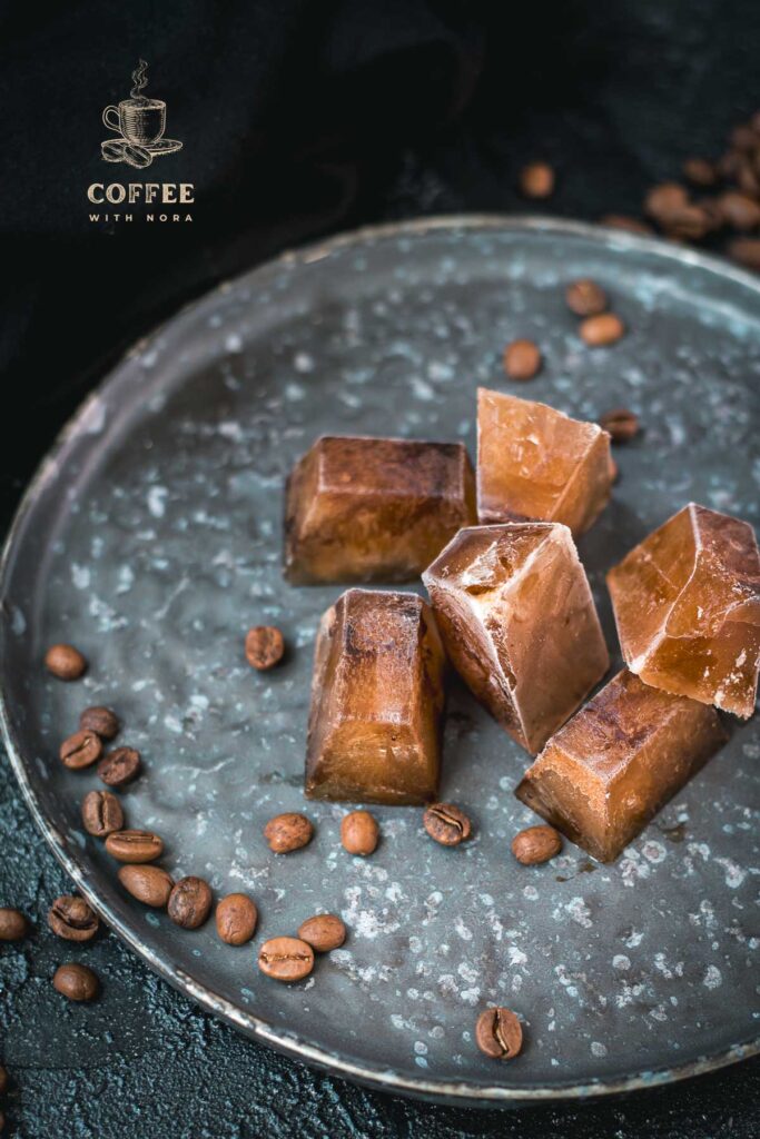 Frozen coffee cubes placed on metal plate next to coffee beans.