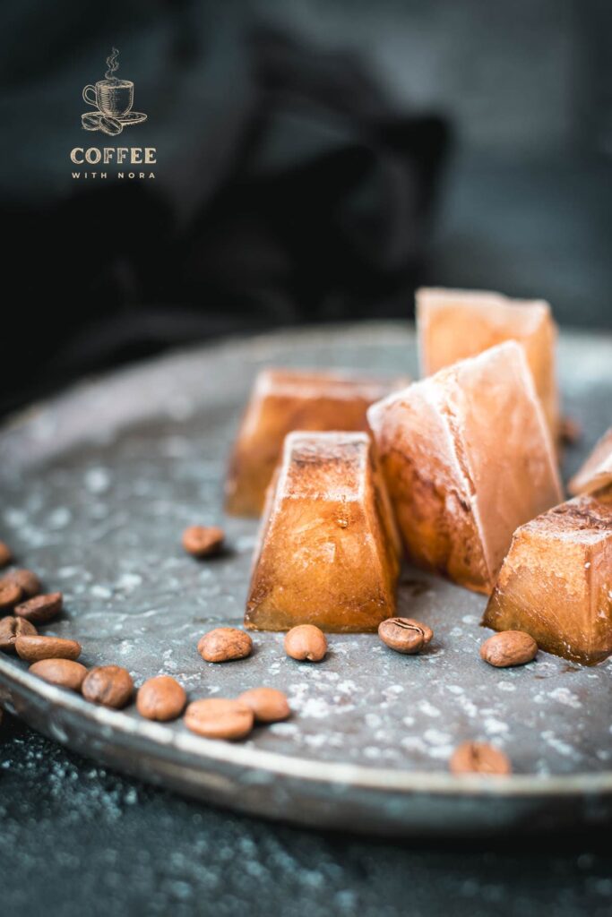 Frozen coffee cubes placed on metal plate next to coffee beans.