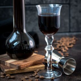 Gorgeous glass filled with homemade coffee liqueur, placed next to preserving jar and jigger.