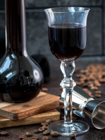 Gorgeous glass filled with homemade coffee liqueur, placed next to preserving jar and jigger.