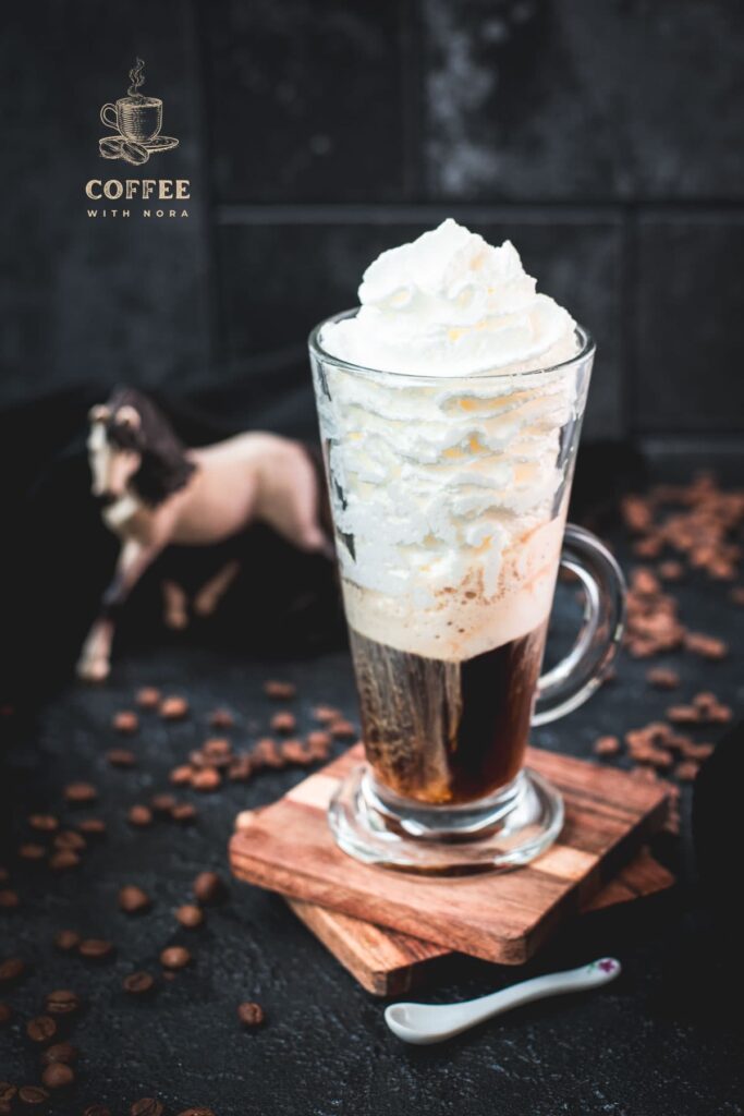 Beautiful tall glass filled with strong coffee and topped with whipped cream. Placed on brown coasters and pretty horse in the background. The Einspänner, a Viennese classic!