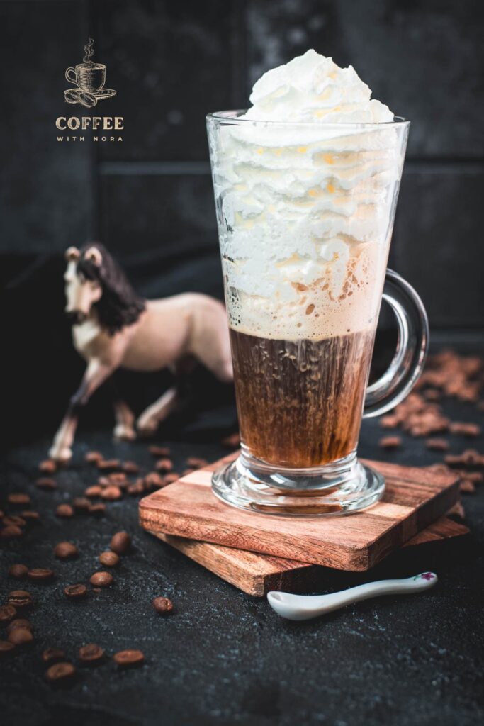 Beautiful tall glass filled with strong coffee and topped with whipped cream. Placed on brown coasters and pretty horse in the background. The Einspänner, a Viennese classic!