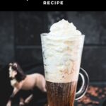 Beautiful tall glass filled with strong coffee and topped with whipped cream. Placed on brown coasters and pretty horse in the background. The Einspänner, a Viennese classic!