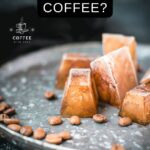 Frozen coffee cubes placed on metal plate next to coffee beans.