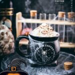 Spooky cauldron coffee mug filled with delicious coffee with rum. Topped with sweetened whipped cream and placed on a black plate surrounded by cobweb.