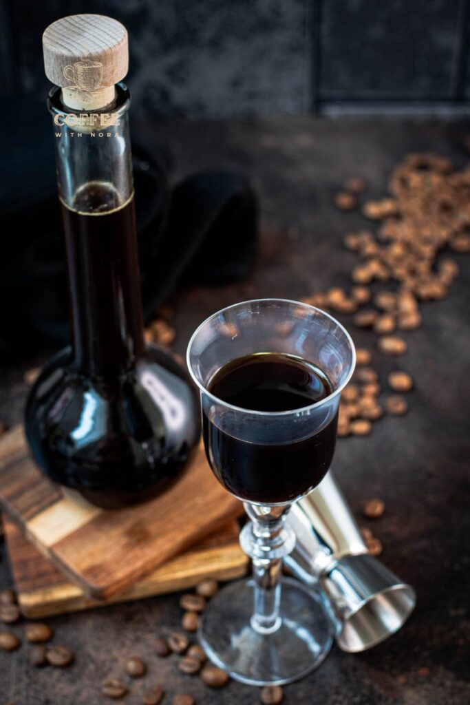 Gorgeous glass filled with homemade coffee liqueur, placed next to preserving jar and jigger.