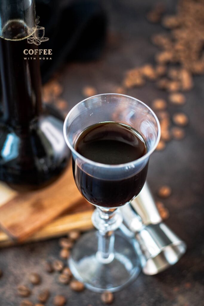 Gorgeous glass filled with homemade coffee liqueur, placed next to preserving jar and jigger.