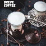 Gorgeous medieval glasses filled with delicious Breve coffee, placed on dark ground next to coffee beans.