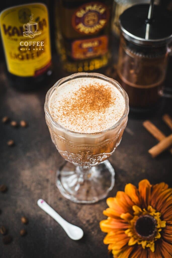 Rich French press Mexican coffee in gorgeous serving glass, placed on brown colored ground, next to orange-colored flower.