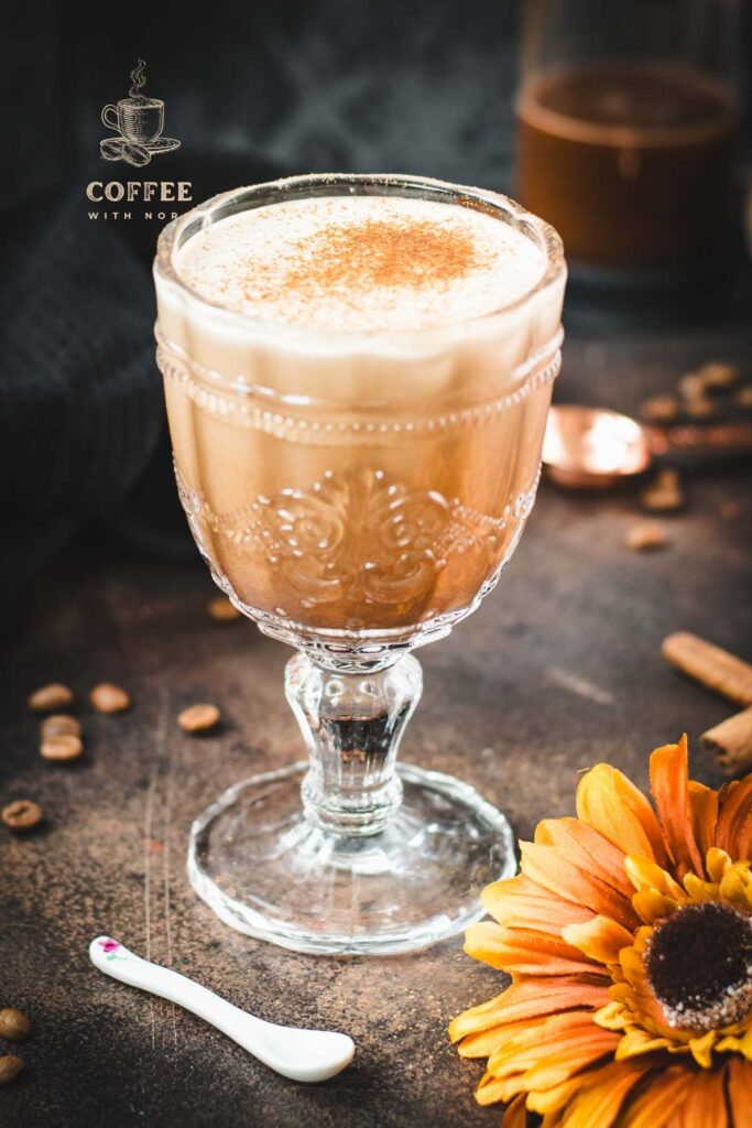 Rich French press Mexican coffee in gorgeous serving glass, placed on brown colored ground, next to orange-colored flower.