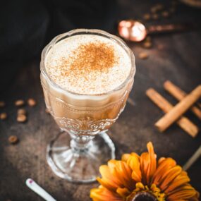 Rich French press Mexican coffee in gorgeous serving glass, placed on brown colored ground, next to orange-colored flower.