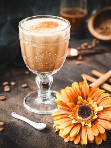 Rich French press Mexican coffee in gorgeous serving glass, placed on brown colored ground, next to orange-colored flower.