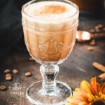 Rich French press Mexican coffee in gorgeous serving glass, placed on brown colored ground, next to orange-colored flower.