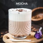 Gorgeous glass, filled with a delicious Mocha, topped with frothed milk, and garnished with chocolate sprinkles. Placed on a small wooden plate next to dark chocolate kisses.