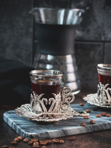 Gorgeous medieval glass filled with delicious specialty coffee placed on marbled plate.