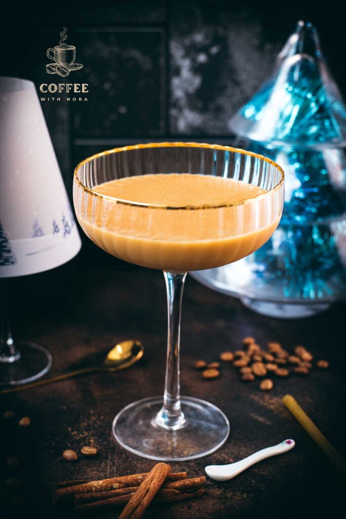 Gorgeous long stemmed cocktail glass with golden rim filled with a Cold Brew Kahlua Eggnog Cocktail, placed on dark ground.