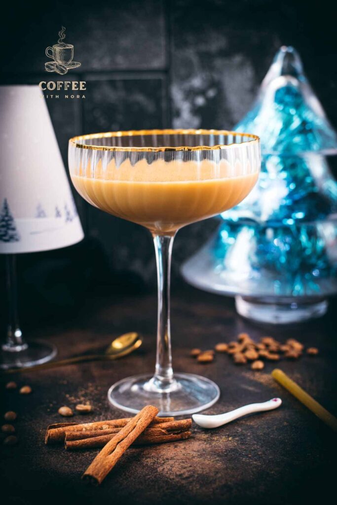 Gorgeous long stemmed cocktail glass with golden rim filled with a Cold Brew Kahlua Eggnog Cocktail, placed on dark ground.