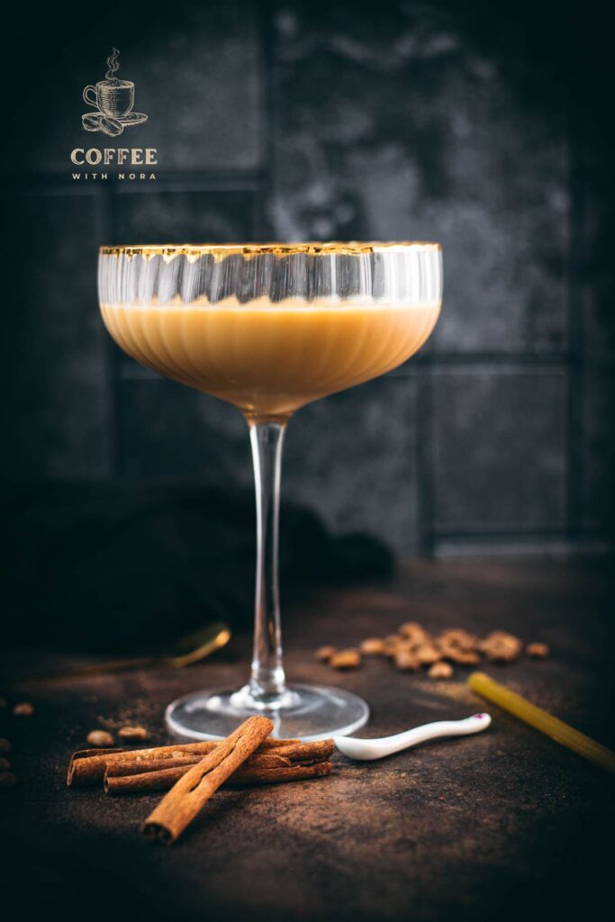 Gorgeous long stemmed cocktail glass with golden rim filled with a Cold Brew Kahlua Eggnog Cocktail, placed on dark ground.