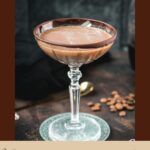 Creamy mocha martini in gorgeous glass, placed on glass coaster on dark ground.