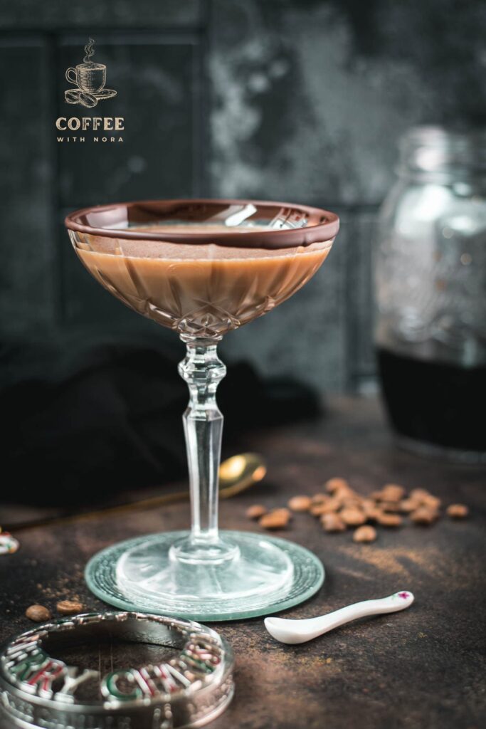 Creamy mocha martini in gorgeous glass, placed on glass coaster on dark ground.