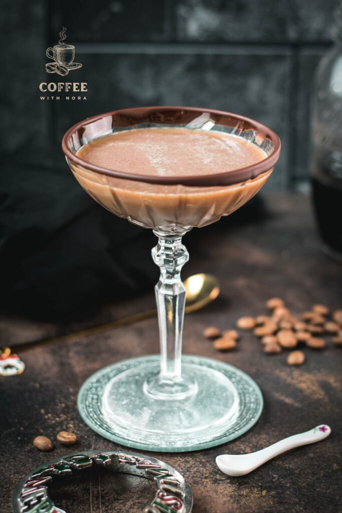 Creamy mocha martini in gorgeous glass, placed on glass coaster on dark ground.