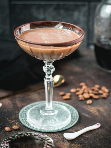 Creamy mocha martini in gorgeous glass, placed on glass coaster on dark ground.