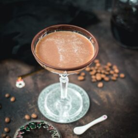 Creamy mocha martini in gorgeous glass, placed on glass coaster on dark ground.