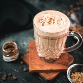 Divine Nutella coffee with homemade Nutella-flavored whipped cream, placed on two wooden coaters on dark ground.