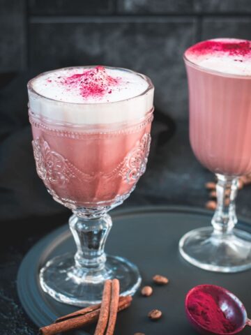 Delicious pink latte filled in gorgeous glasses placed on a dark plate.