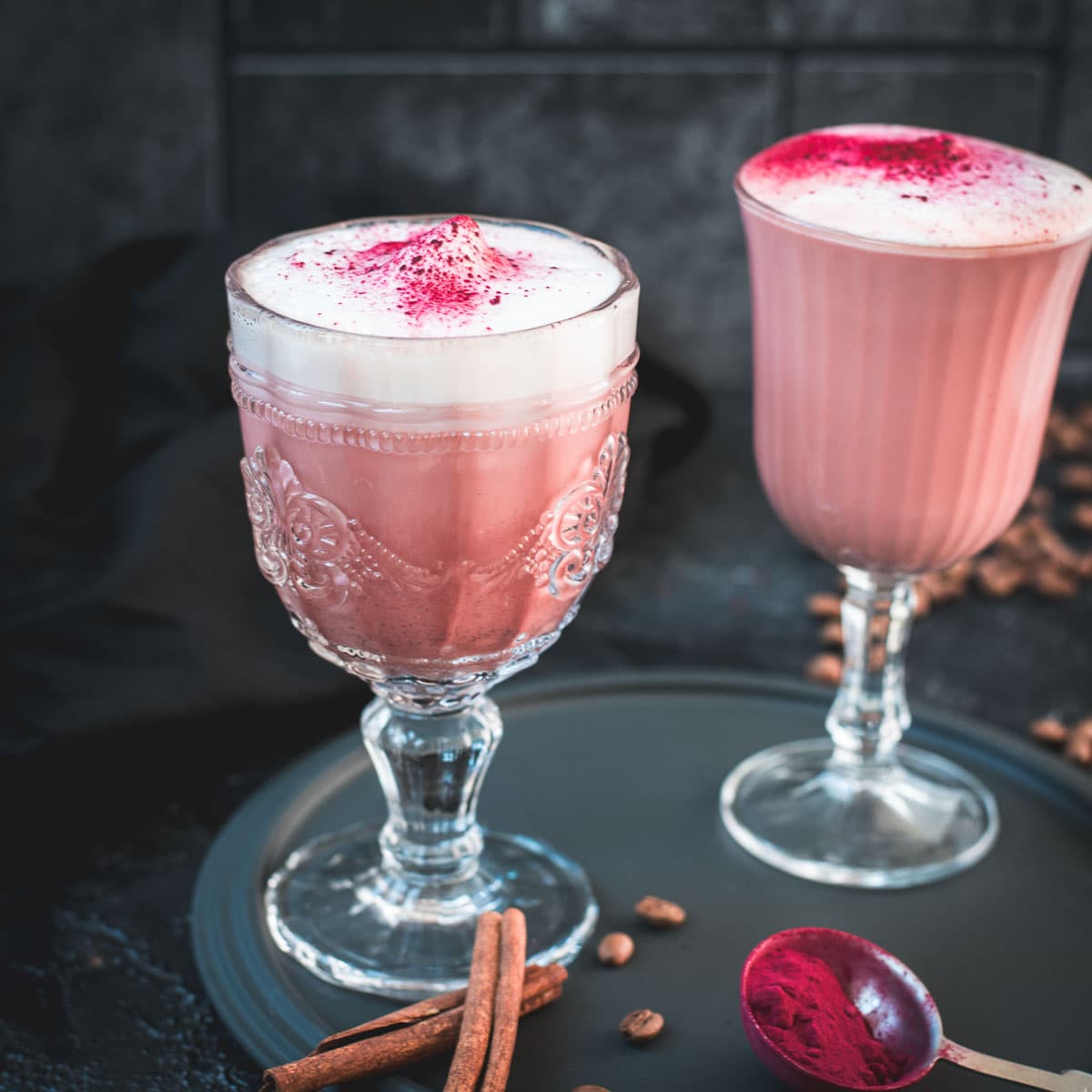 Delicious pink latte filled in gorgeous glasses placed on a dark plate.