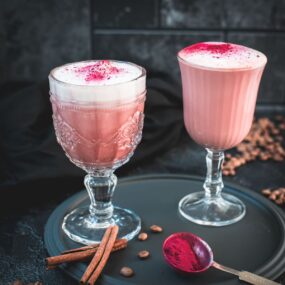 Delicious pink latte filled in gorgeous glasses placed on a dark plate.