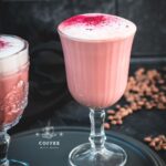 Delicious pink latte filled in gorgeous glasses placed on a dark plate.