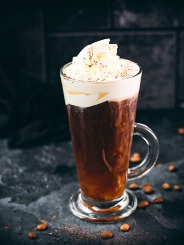 Delicious Irish coffee, topped with whipped cream and sprinkled with cocoa powder, placed on black slate plate.