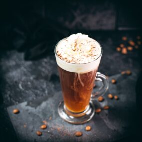 Delicious Irish coffee, topped with whipped cream and sprinkled with cocoa powder, placed on black slate plate.