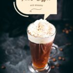 Delicious Irish coffee, topped with whipped cream and sprinkled with cocoa powder, placed on black slate plate.