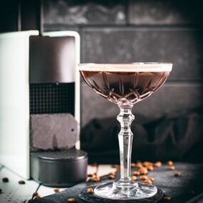 Cocktail glass, filled with a decadent Nespresso martini. Placed on a black slate plate, next to coffee beans.