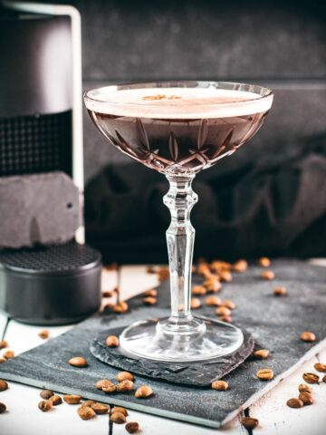 Cocktail glass, filled with a decadent Nespresso martini. Placed on a black slate plate, next to coffee beans.