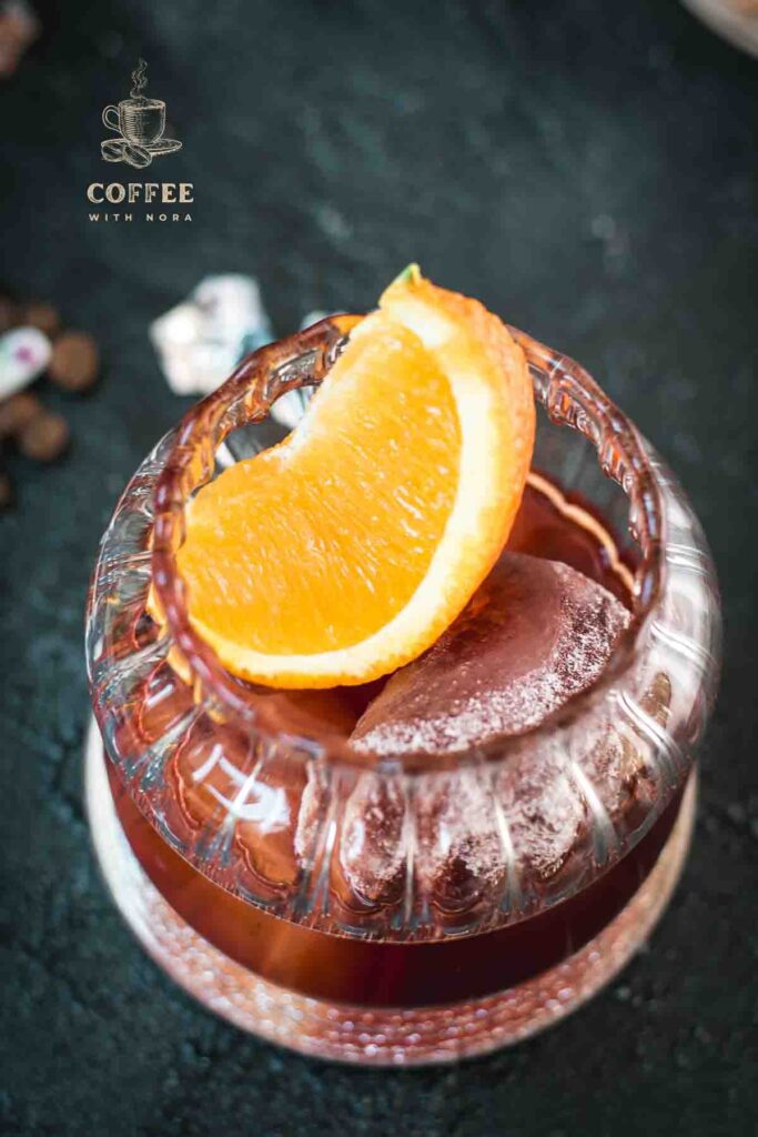 Gorgeous rocks glass, filled with a delicious cold brew negroni, garnished with an orange slice, and placed on a mirrored coaster.