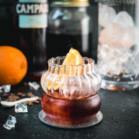 Gorgeous rocks glass, filled with a delicious cold brew negroni, garnished with an orange slice, and placed on a mirrored coaster.