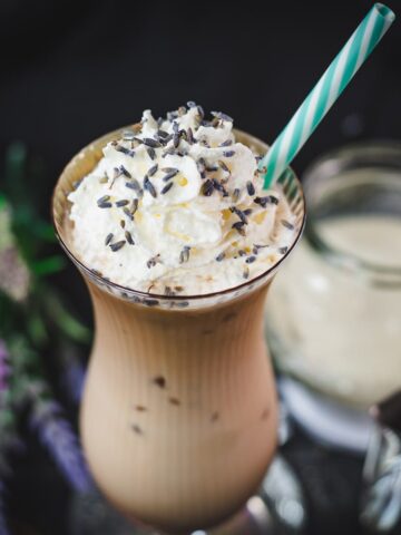 Gorgeous Hurricane glass, filled with crushed lavender iced latte, topped with whipped cream and sprinkled with lavender buds. Served with a turquoise white striped drinking straw.